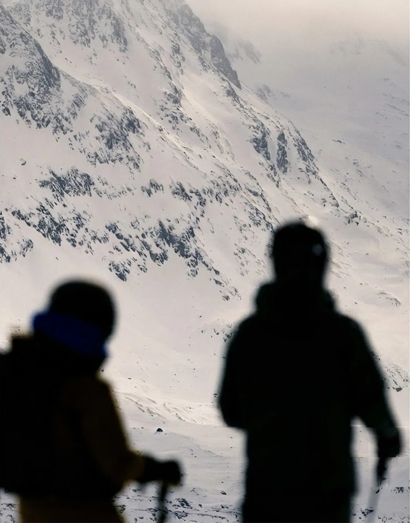 Two skiers looking out over a snow-covered mountain face